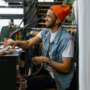 Cheerful man in orange beanie, inside a trendy clothing boutique, smiling at the counter.