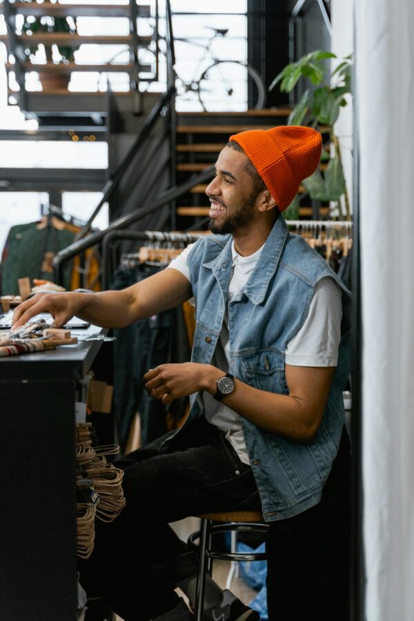 Cheerful man in orange beanie, inside a trendy clothing boutique, smiling at the counter.