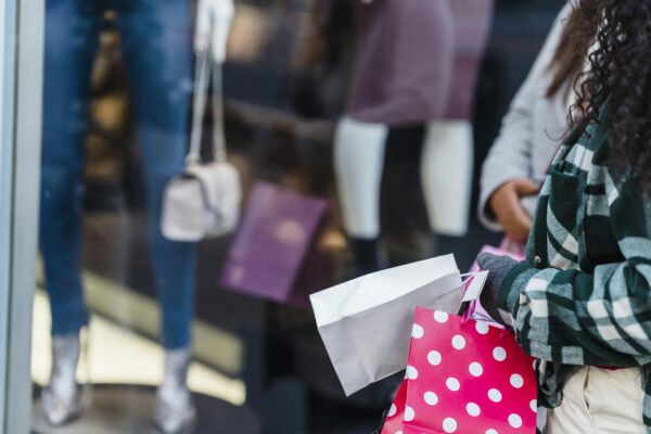 Crop anonymous women friends in stylish clothes standing with shopping bags near counter of boutique in daytime