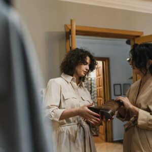 Two women engaged in shopping discussion over a leather boot in a stylish fashion boutique.